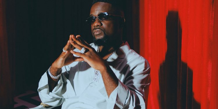 Sarkodie in a white outfit in front of a red curtain, shared with his announcement of the single Cold
